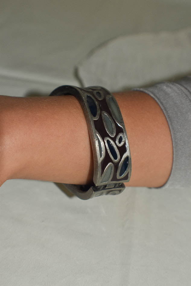 Close-up of a wrist wearing a dark  bangle with metallic accents on a light gray background.