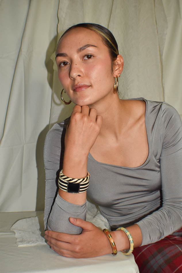 Woman wearing a gray long-sleeve top with visible jewelry against a plain background