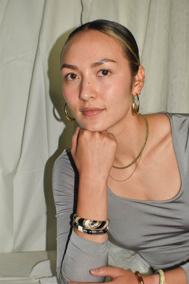 Woman wearing a gray top with visible jewelry against a neutral background
