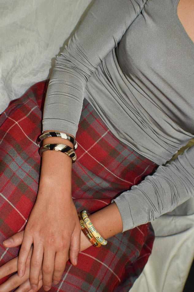 Person wearing a gray long-sleeve top and red plaid skirt with visible jewelry.