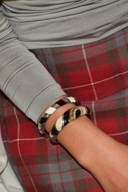 Person wearing a gray long-sleeve top and red plaid skirt with multiple metal bracelets on a neutral background