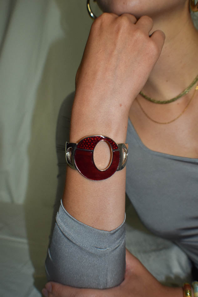 Person wearing a red and silver bracelet on a neutral background