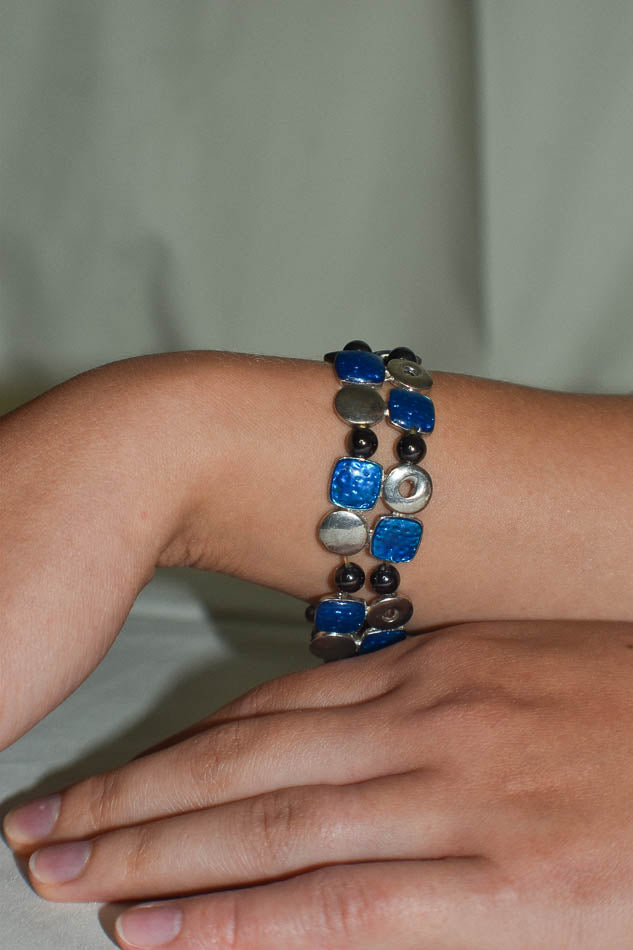Close-up of a hand wearing a colorful beaded bracelet on a neutral background