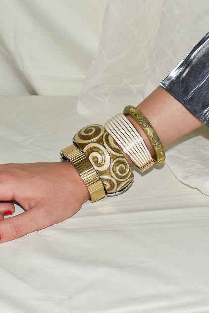 Hand wearing gold and white patterned bracelets on a white fabric background