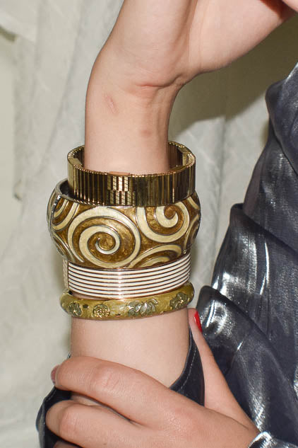 Close-up of a wrist wearing multiple gold and silver bracelets with a metallic sleeve.