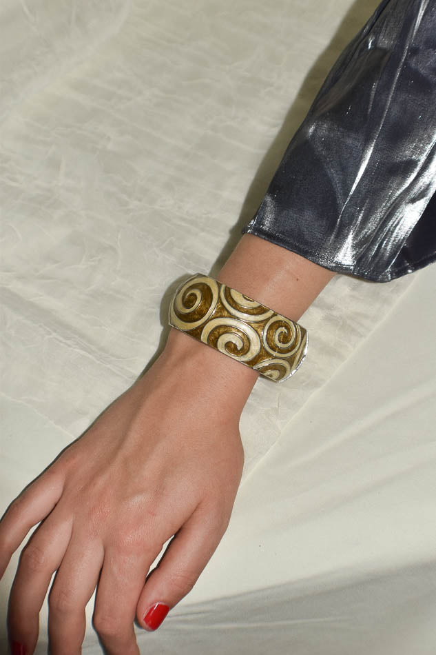 Hand wearing a gold and white patterned bracelet on a neutral background