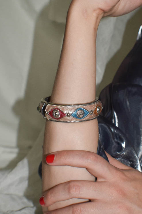 Close-up of a hand wearing a decorative bracelet with red, blue, and gold elements.