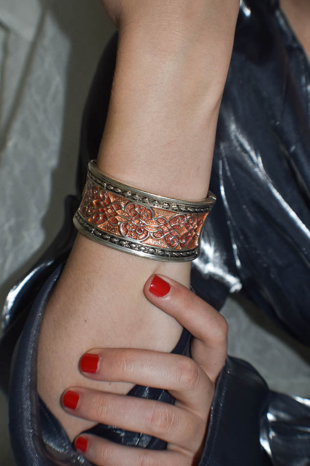 Hand wearing a decorative bracelet with red nail polish on a blurred background