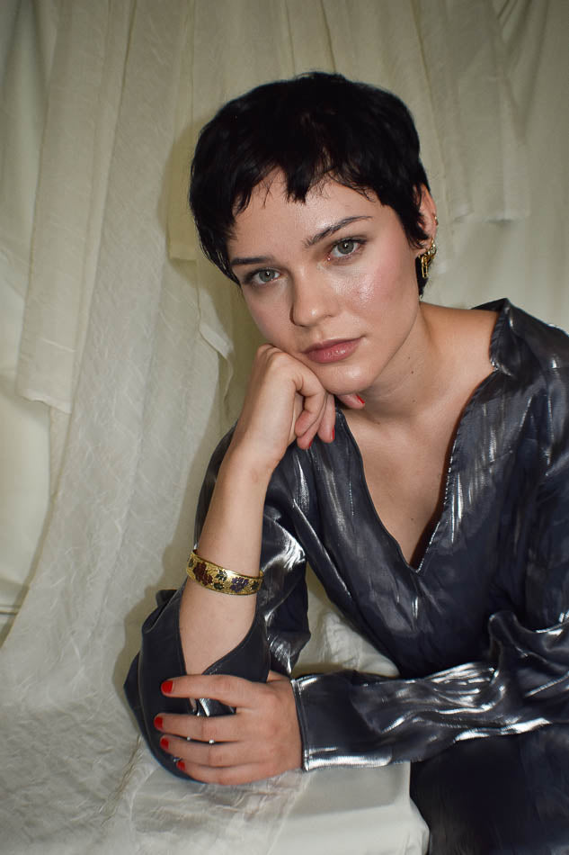 Woman wearing a shiny silver jacket against a light curtain background