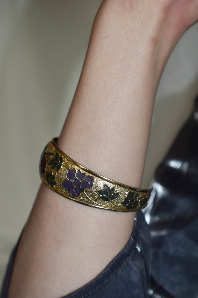 Gold bracelet with purple design on a wrist against a neutral background