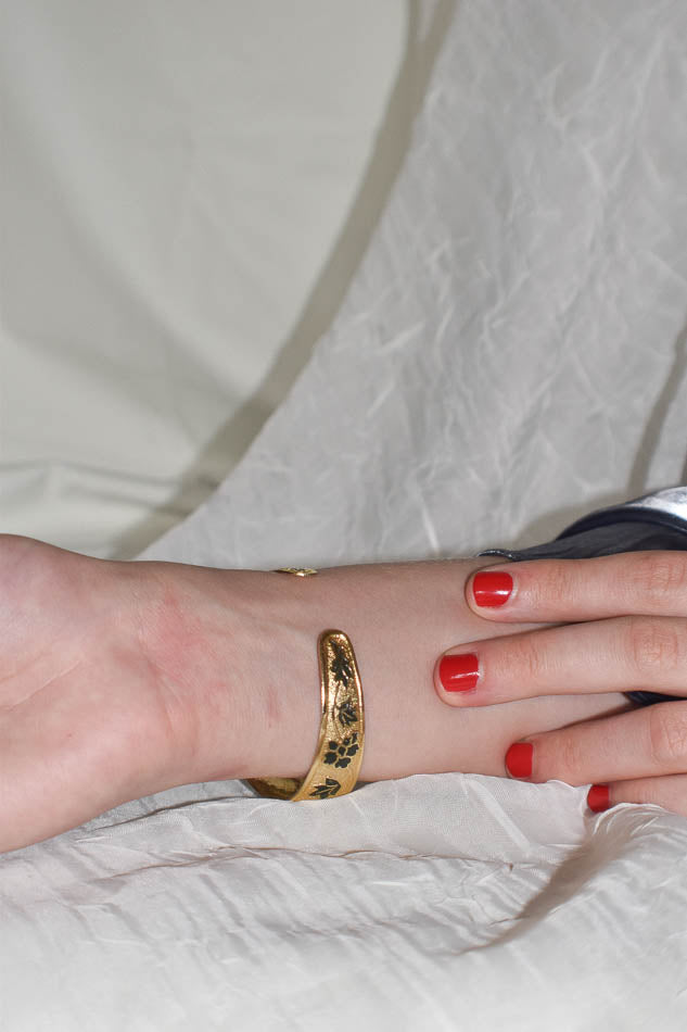 Gold bracelet on a wrist with red nail polish against a neutral background