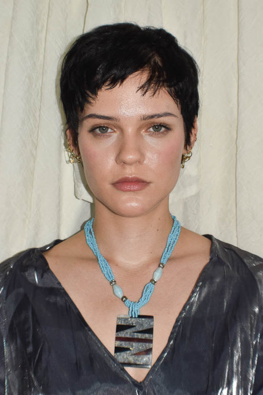 Woman wearing a blue necklace with a pendant against a neutral background
