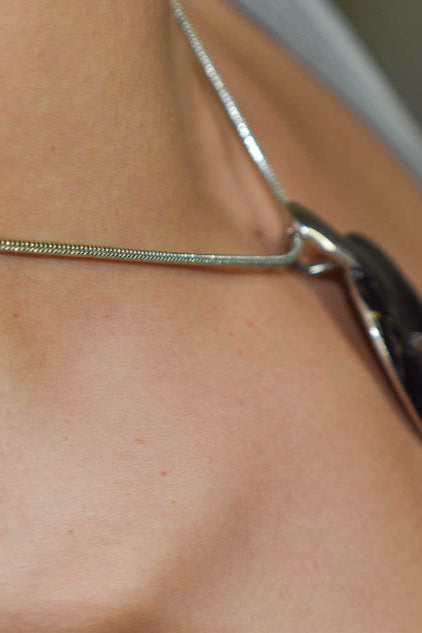 Close-up of a person wearing a silver necklace with a blurred background