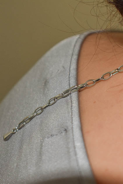 Close-up of a silver chain necklace on a person wearing a gray shirt.