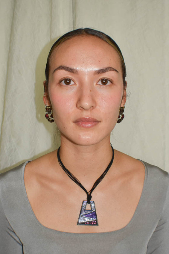 Woman wearing a gray top and necklace with a pendant against a plain background