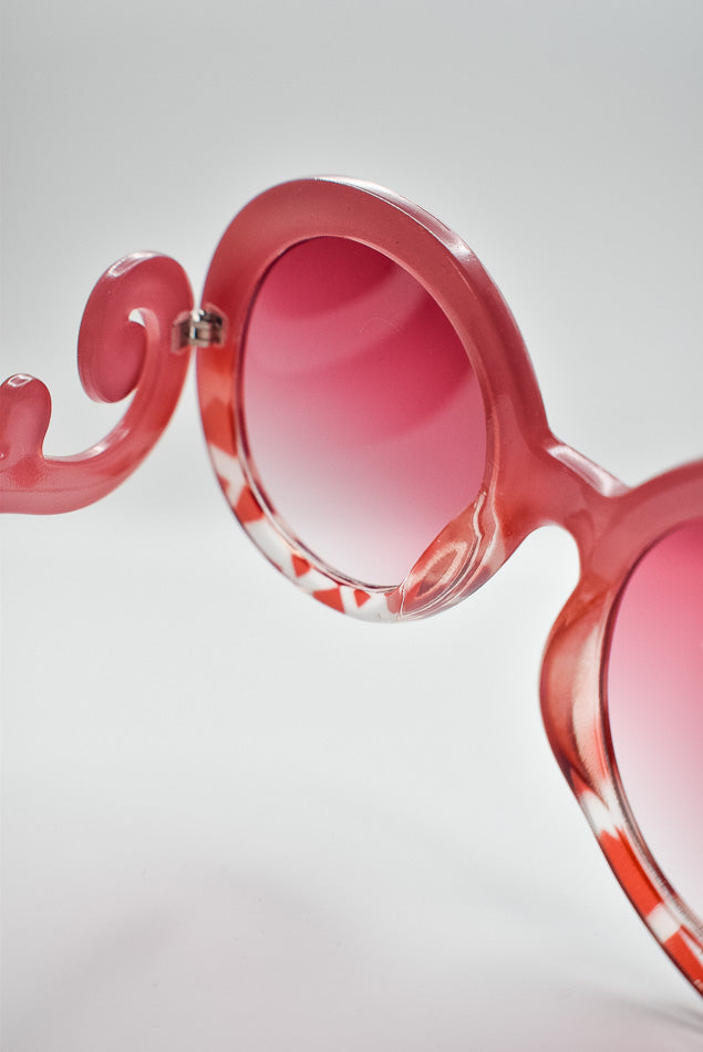 Sunglasses with pink lenses and red frames on a light gray background