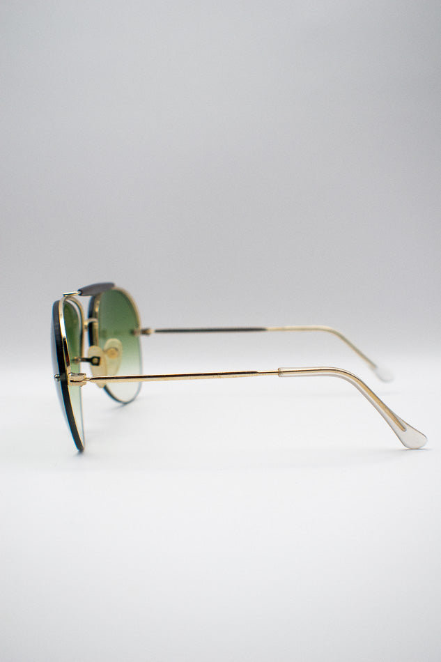 Gold-framed sunglasses with green lenses on a light gray background
