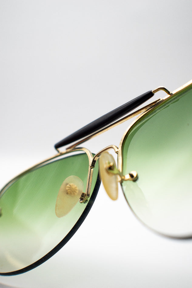 Aviator sunglasses with green lenses and gold frames on a white background