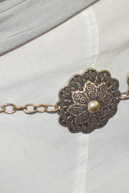 Decorative belt with floral patterns and chain details on a light-colored garment.