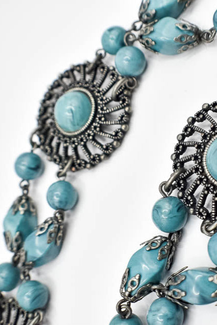 Turquoise beaded necklace with silver floral designs on a white background