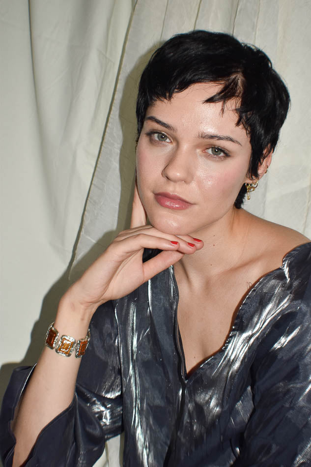 Woman with short black hair wearing a metallic silver top against a neutral background