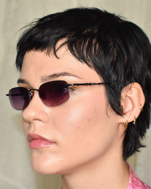 Close-up of a person with short black hair wearing sunglasses and gold.earrings.