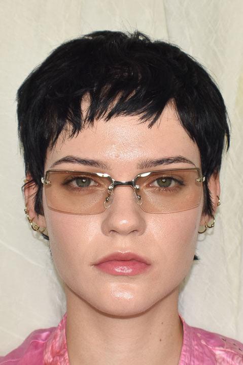 A person wearing clear half rim Y2K sunglasses with a sleek silver frame and slim arms, sitting against a neutral background.